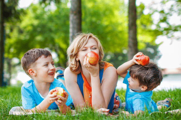 mom laying on the ground with two boys eating apples