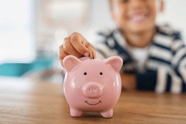 little boy adding money to piggy bank