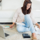 woman smiling paying bills on the floor with laptop