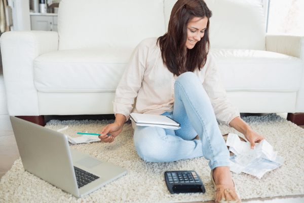 woman smiling paying bills on the floor with laptop