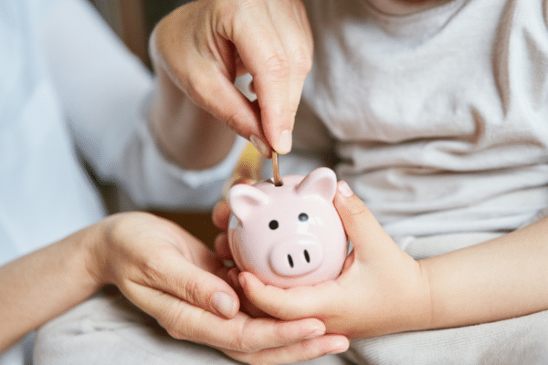 child and adult putting money in piggy bank