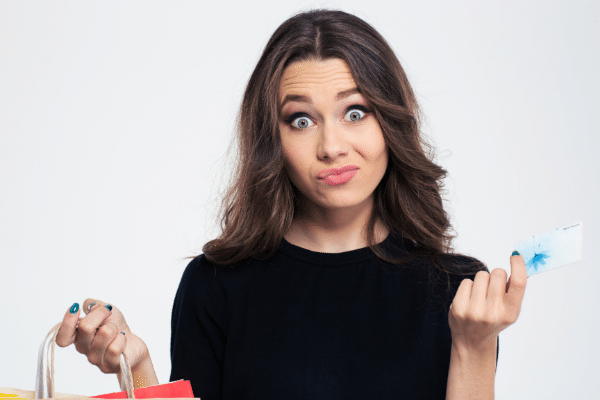 woman black shirt shopping bag in one hand credit card in other shrugging shoulders