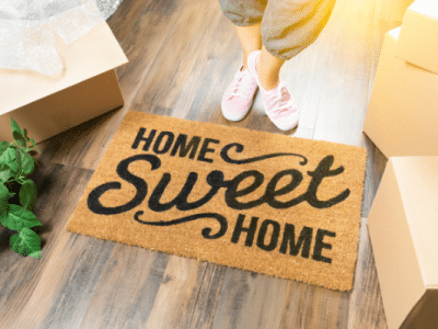 home sweet home door mat woman standing next to it moving boxes