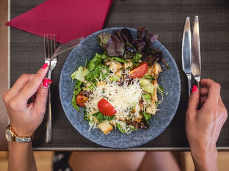 salad on blue plate and red napkin on wooden lap tray | woman's hands with red finger nails holding utensils