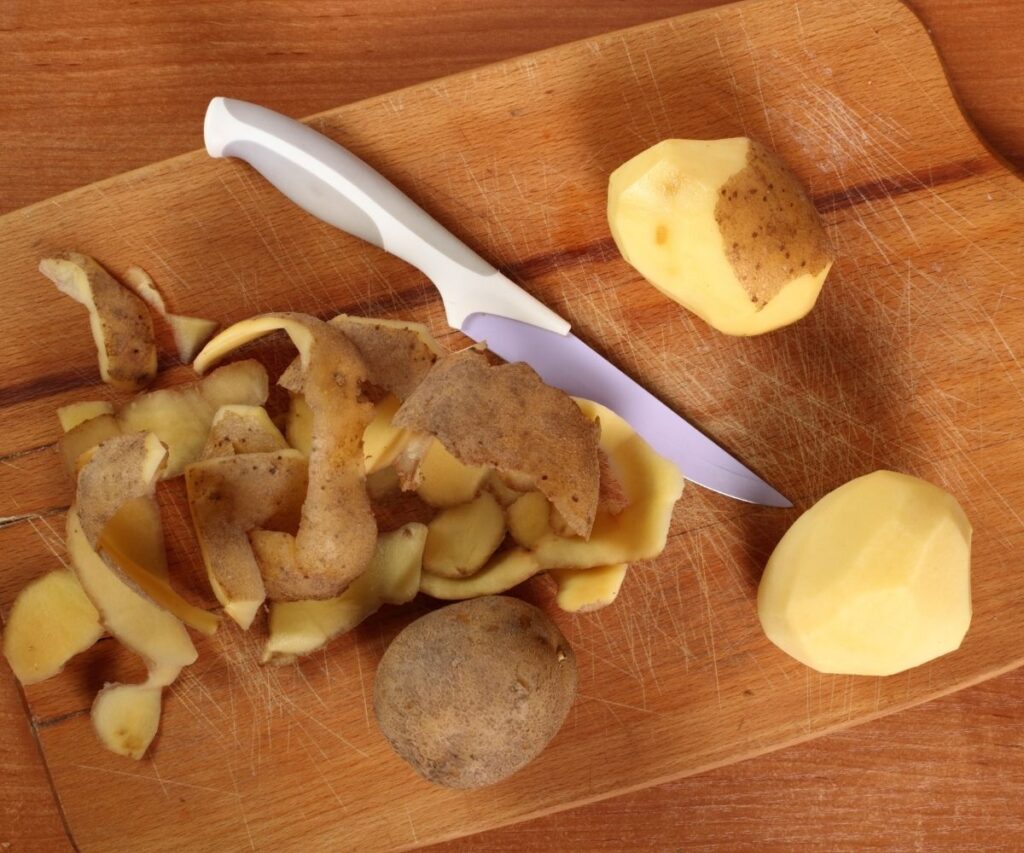 potato peels and peeled potatoes and knife on chopping board