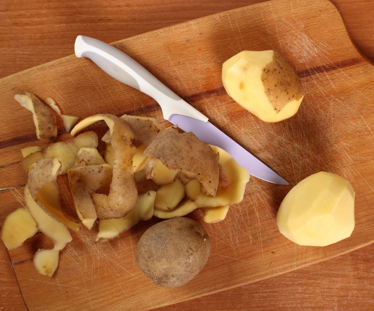 potato peels and peeled potatoes and knife on chopping board