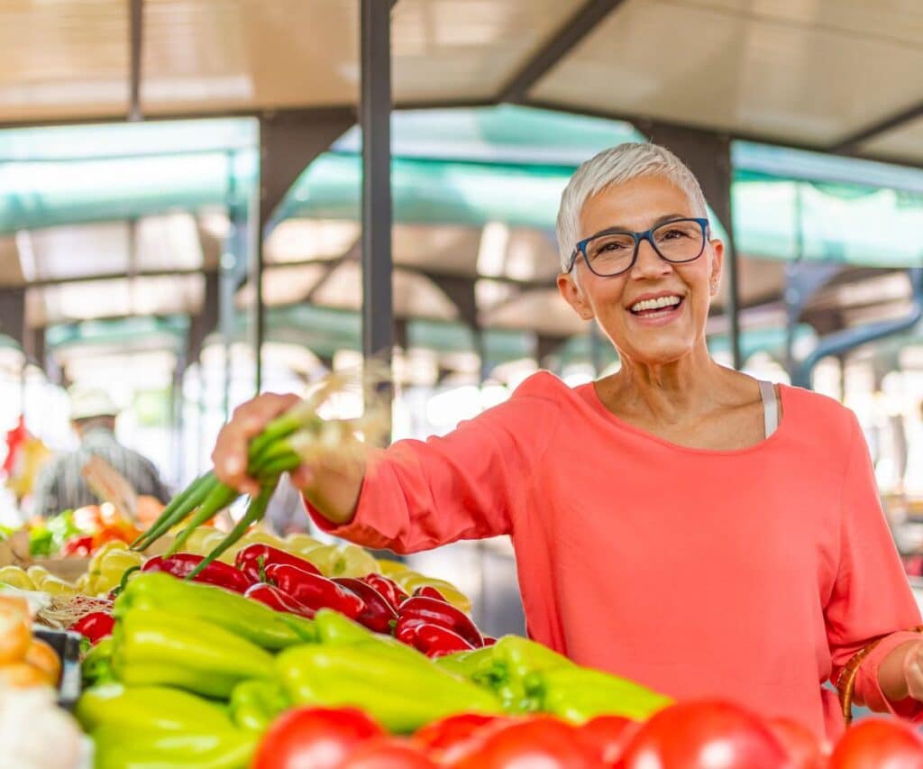 smiling woman with gray hair and bright peach shirt shopping at a farmer's market