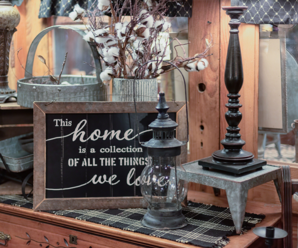 A chalkboard sign with a lantern and candle holder on a sideboard with other farmhouse decor items