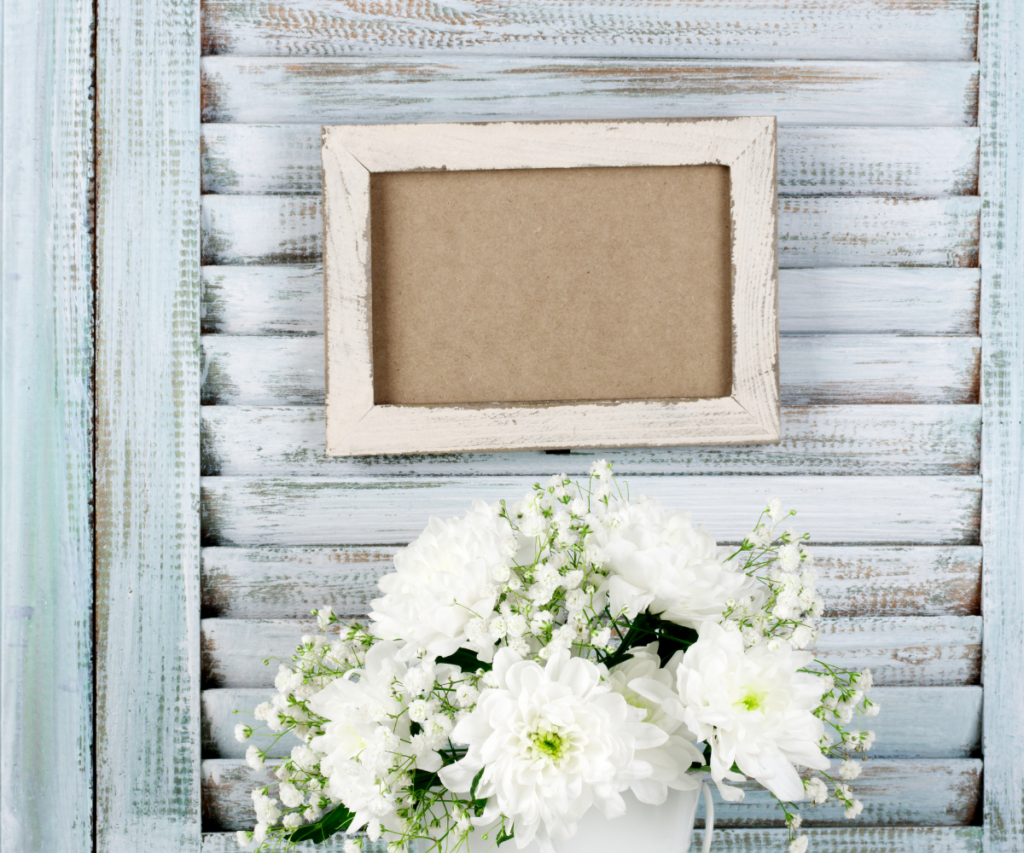 Rustic white shutter with an empty picture frame and white flowers in front of it