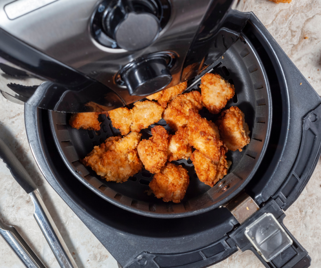 An air fryer with basket open and chicken pieces inside